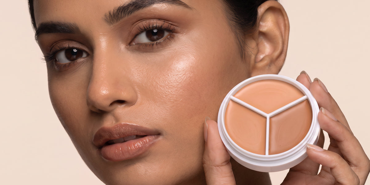 A woman dotting concealer on her cheekbone, the three-colour compact in her hand