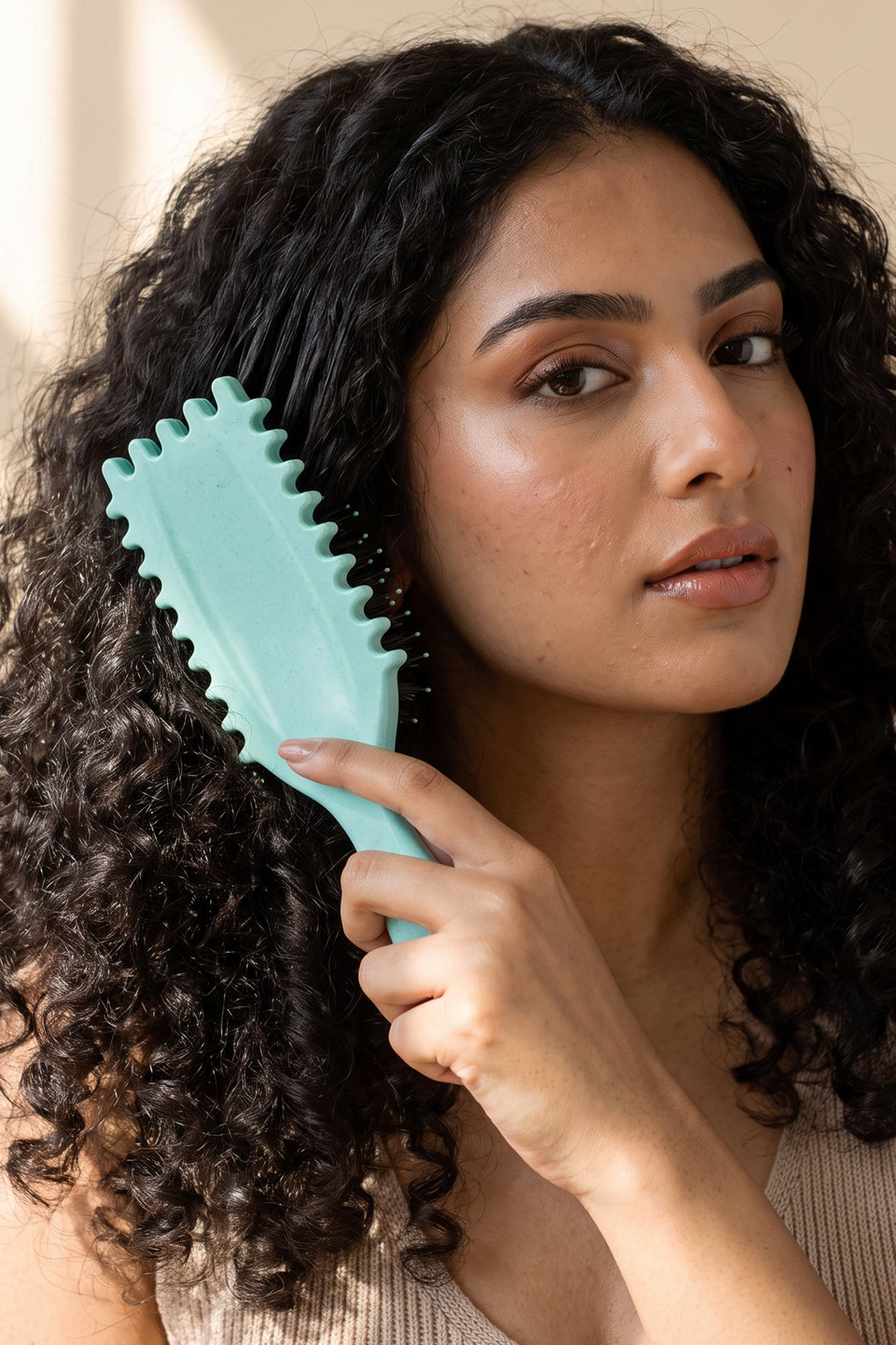 A woman with long dark curls brushing them with the teal Gleva curl brush