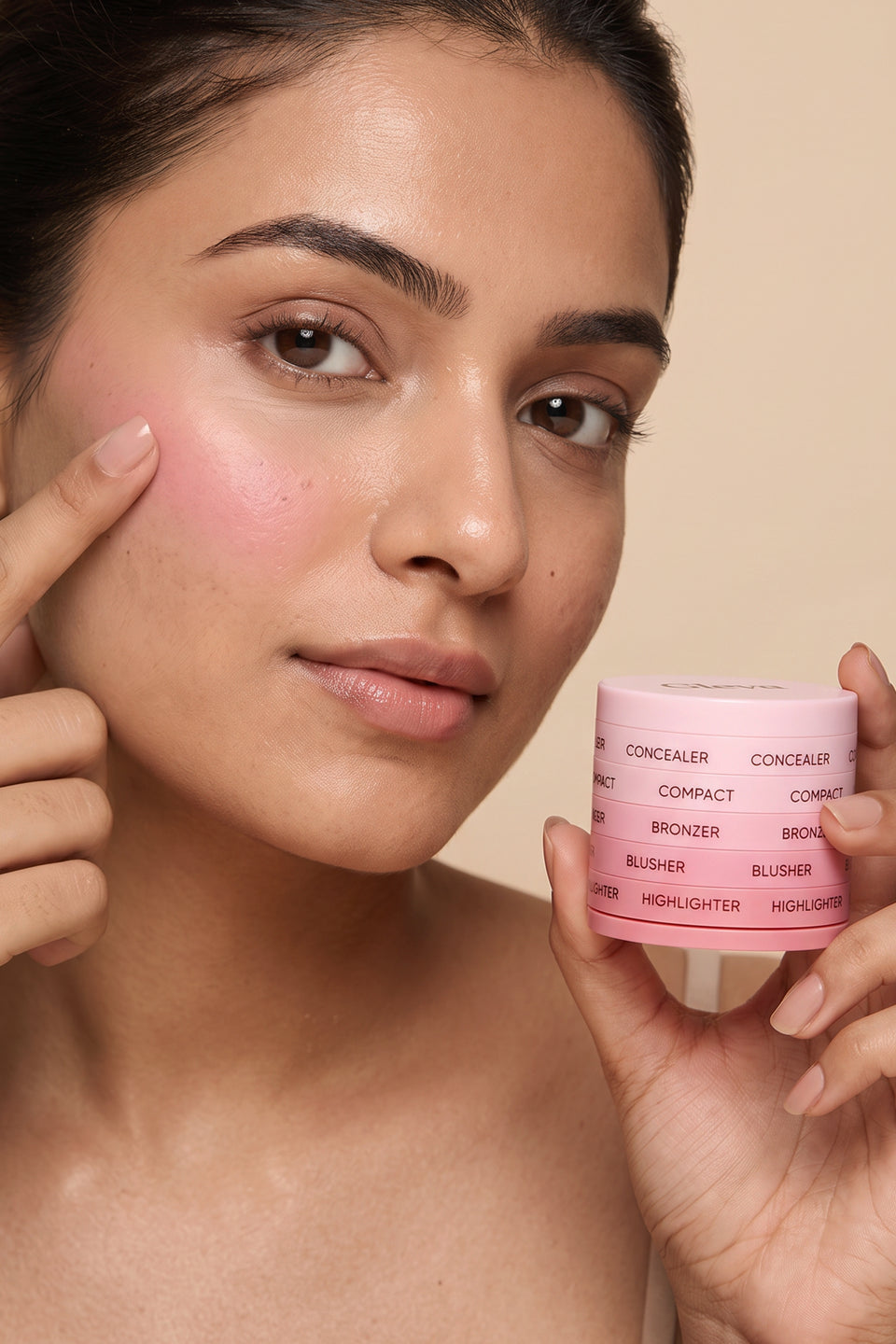 A woman dabbing blusher on her cheek with a fingertip, holding the pink 5-in-1 Makeup Stack